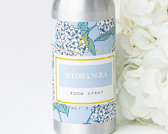Room spray bottle with floral label next to white flowers on a light background