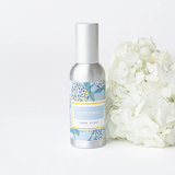 Room spray bottle with floral label next to white flowers on a light background