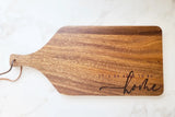 Wooden cutting board with 'It's so good to be home' text on a white marble background