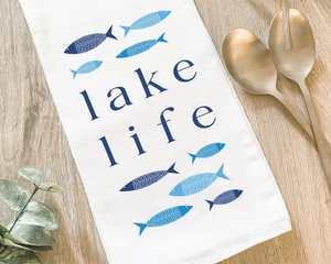 Blue 'Lake Life' kitchen towel  Form and function come together in this fun, flour-sack tea towel. Featuring a hand-drawn design, each towel has the phrase, "Lake Life," in dark blue letters. The phrase is surrounded by fish in light blue and dark blue shades. This would be a perfect gift for a lake enthusiast.&nbsp;  This item is proudly made in the USA.  Materials: Cotton  Dimensions: 27" wide x 27" long  Care: This item is machine washable.