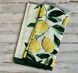 Two kitchen towels with lemon and leaf pattern on a wooden surface