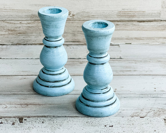 Sold in pairs, these wooden candlesticks are painted in a soft pale blue and accented with a hand-rubbed charcoal antiquing glaze to bring out their farmhouse style. They are finished with a matte wax sealer for durability. Each candle holder holds a standard size taper candle.