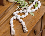 This garland features wooden beads strung on a jute rope with alternating large white beads and small mint blue beads. Either end of the garland is adorned with decorative cream-colored, leather-like tassels. String this garland upon a tabletop or around spring greenery for a cheery look.

Materials:
Wood, jute, faux leather

Dimensions:
49" long