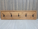 Wooden coat rack with five hooks against a wooden wall.