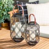Two decorative lanterns with candle holders on a wooden surface outdoors.
