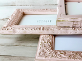 Decorative ornate pink and gold picture frames on a wooden surface