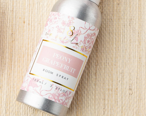 Peony Grapefruit room spray bottle with floral label on a woven surface