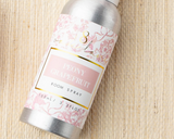 Peony Grapefruit room spray bottle with floral label on a woven surface