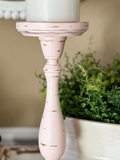 Pink candle holder with a white candle on a surface with greenery in the background