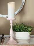 Pink candle holder with a lit candle next to a potted plant on a surface.