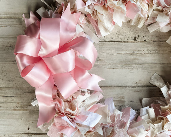 Pink and beige ribbon wreath on a wooden surface