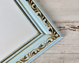 Decorative mirror frame with intricate gold designs on a wooden surface