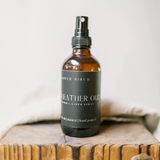 Bottle of Leather Oud room and linen spray on a wooden surface with a neutral background