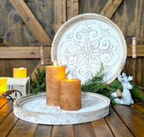 Decorative wooden tray with candles and a decorative plate on a wooden surface.
