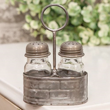 Galvanized metal salt &amp; shaker set caddy

This caddy is a vintage-inspired piece made of galvanized silver metal with a raised pattern and a circular handle attached to the middle. Either side of the caddy holds a glass seasoning shaker with a screw-top metal lid with holes at the top. Fill these shakers with salt and pepper, and display this caddy on any tabletop, riser, or other kitchen surface for easy access with a decorative, farmhouse-inspired touch.

Materials:
Metal, glass