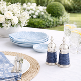 Outdoor table setting with blue plates, silver salt and pepper shakers, and white flowers.
