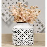 This short vase is a decorative container made of metal with a distressed white finish. It has a black rim and features a raised black floral pattern, offering a chic, yet vintage touch. This vase is ideal for year-round or seasonal use, displayed filled with florals, greenery, and decorative picks and sprays. 