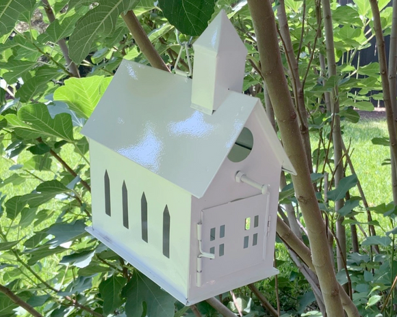 White birdhouse attached to a tree branch with green leaves in the background