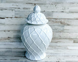 White ceramic jar with a textured design and lid on a wooden surface