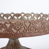 Decorative metal cake stand with intricate patterns on a white background
