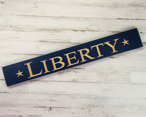 Liberty, Americana, Fourth of July, Patriotic, Navy, Blue, Military, JaBella Designs Show of your patriotism this summer with this rustic wooden wall hanging. It features the word “Liberty” flanked by two stars, all of which are engraved onto a long board that has been painted and distressed in navy blue. This would make a great gift for&nbsp;a military-themed man cave or garage.  This item is proudly made in the USA.