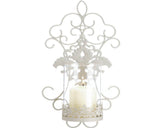 A cream-colored ornate wall sconce with intricate scrollwork and lace, designed to hold a pillar candle.